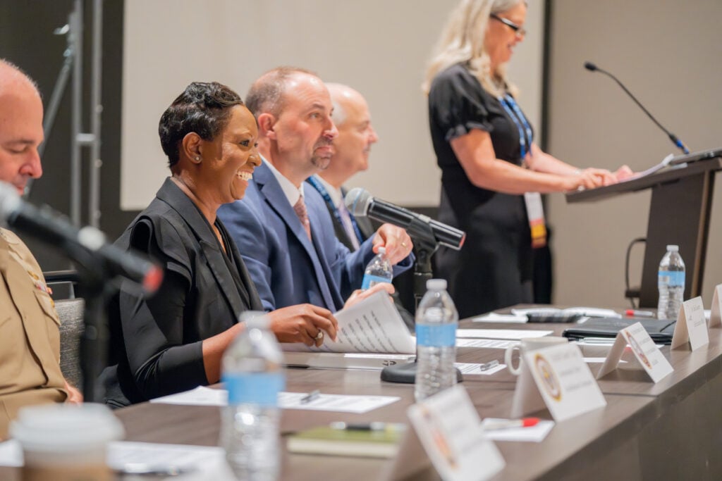 Panel of six professionals seated and standing at conference table during presentation