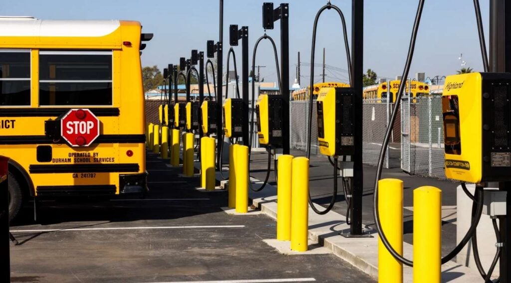 Yellow school buses lined up at electric charging stations with black charging cables