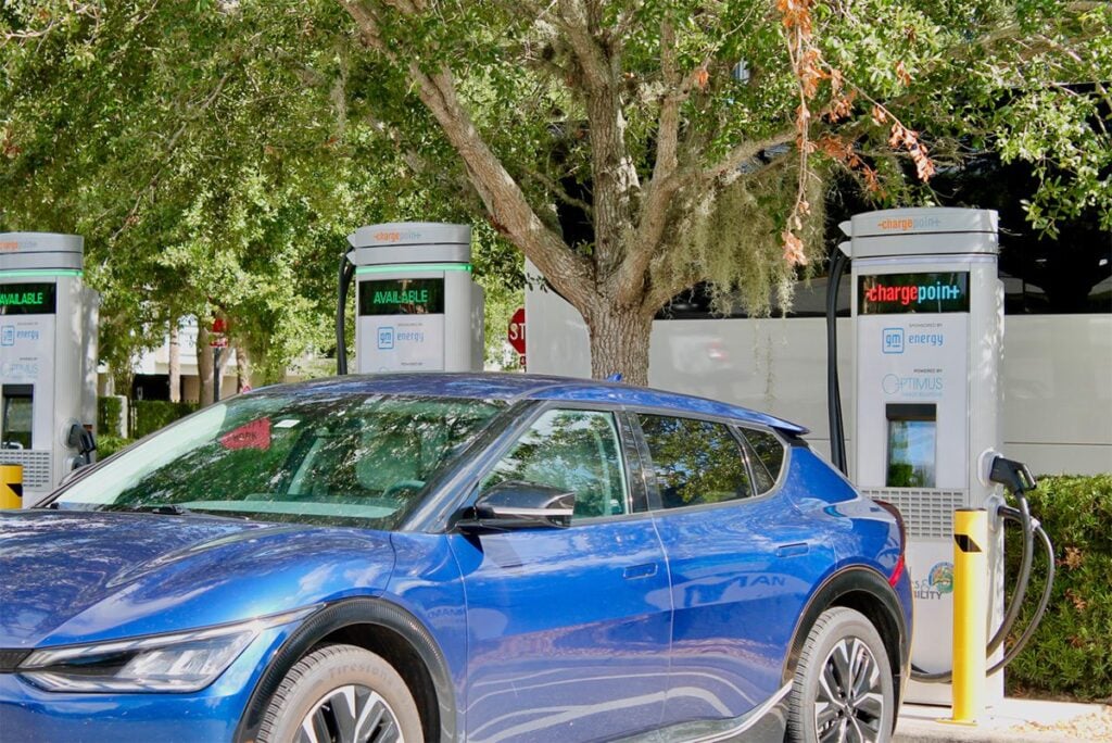 Blue electric vehicle charging at ChargePoint station under trees