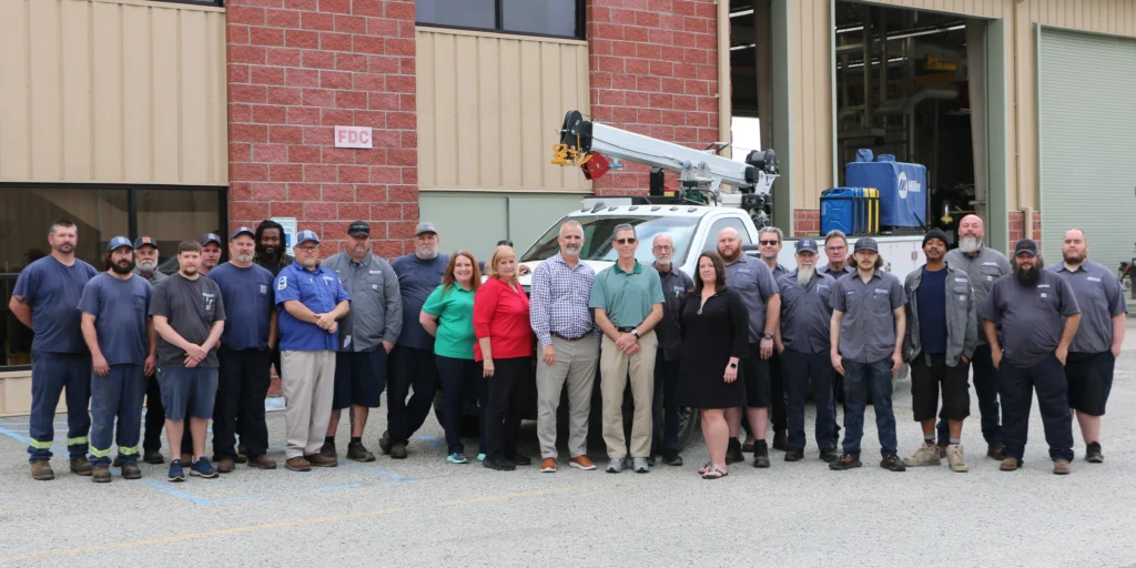 About two dozen Charleston County fleet technicians and staff standing for a group photo outside the maintenance shop, with a crane-equipped service truck behind them