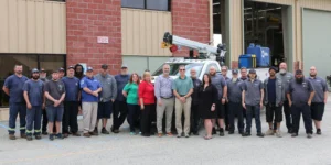 About two dozen Charleston County fleet technicians and staff standing for a group photo outside the maintenance shop, with a crane-equipped service truck behind them