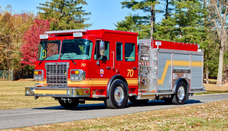 A red Spartan custom pumper fire engine marked unit 70 parked on a road lined with autumn trees