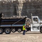 White Freightliner dump truck with hydraulic bed raised, worker standing beside vehicle