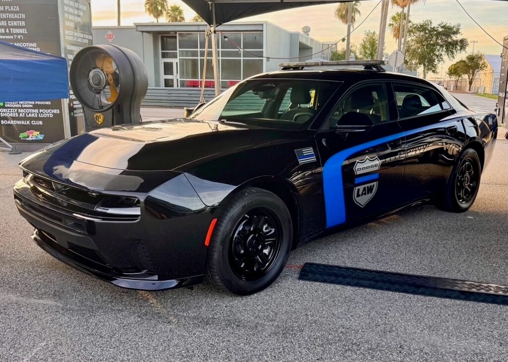 Black Dodge Charger PPV prototype with blue stripe, Dodge Law shield decal and roof light bar, parked under a canopy.