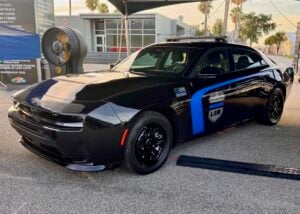Black Dodge Charger PPV prototype with blue stripe, Dodge Law shield decal and roof light bar, parked under a canopy.