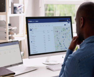 Person viewing FIRST Student HALO fleet management dashboard with map and vehicle tracking data on monitor