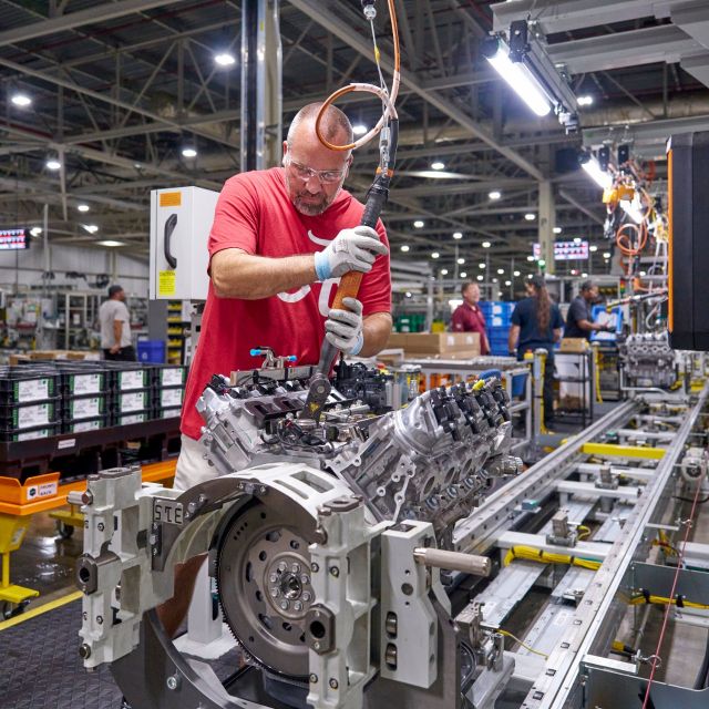 Worker assembling vehicle engine on manufacturing assembly line in industrial factory