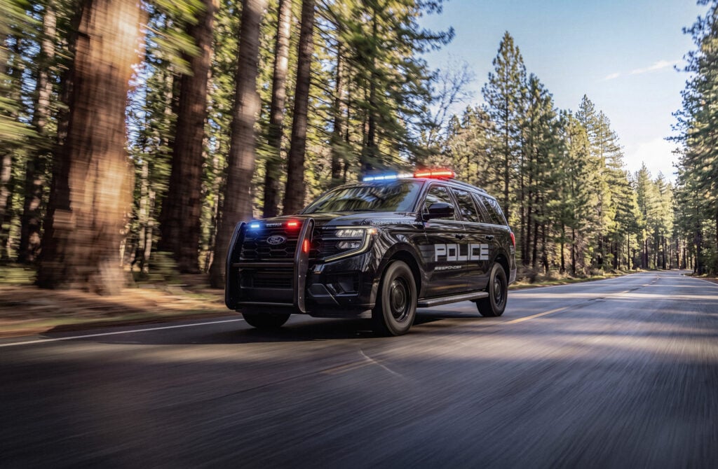 Black Ford Police Expedition driving on forest road with lights activated
