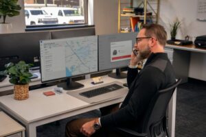 Fleet manager reviews mapping software on dual monitors at office desk