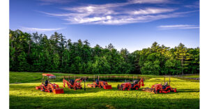 Red compact tractors arranged in a circle on green grass near trees and water
