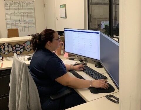 Woman at desk working on computer in small office workspace with supplies and window