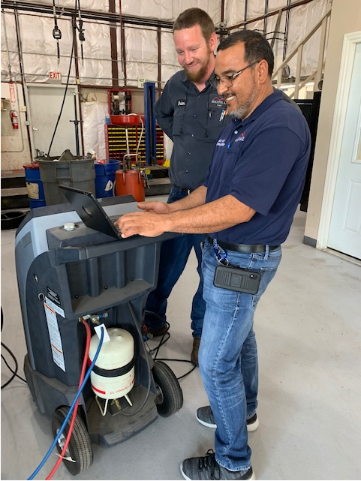 Two technicians operate a diagnostic machine in an industrial garage workshop setting
