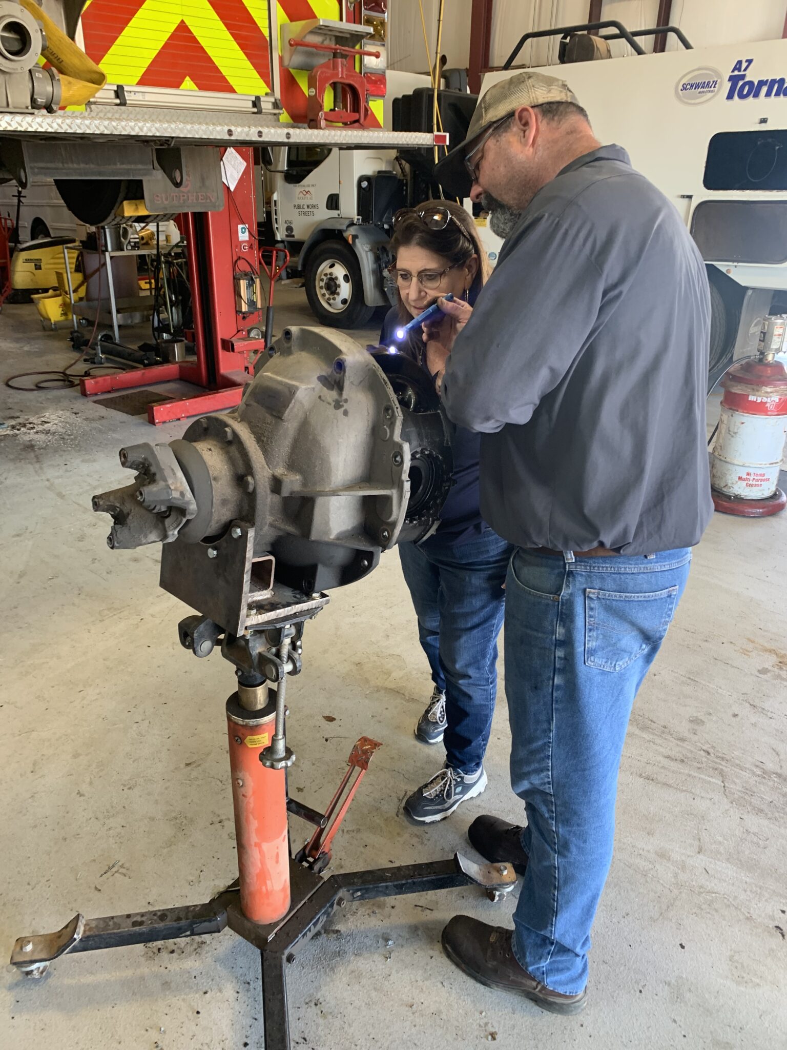 Instructor and trainee examining brake assembly on hydraulic lift in fleet maintenance garage