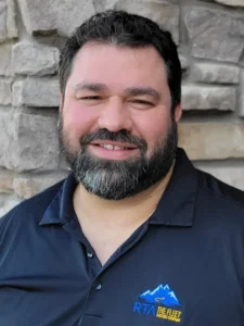 Man in navy polo shirt with mountain logo standing in front of stone building