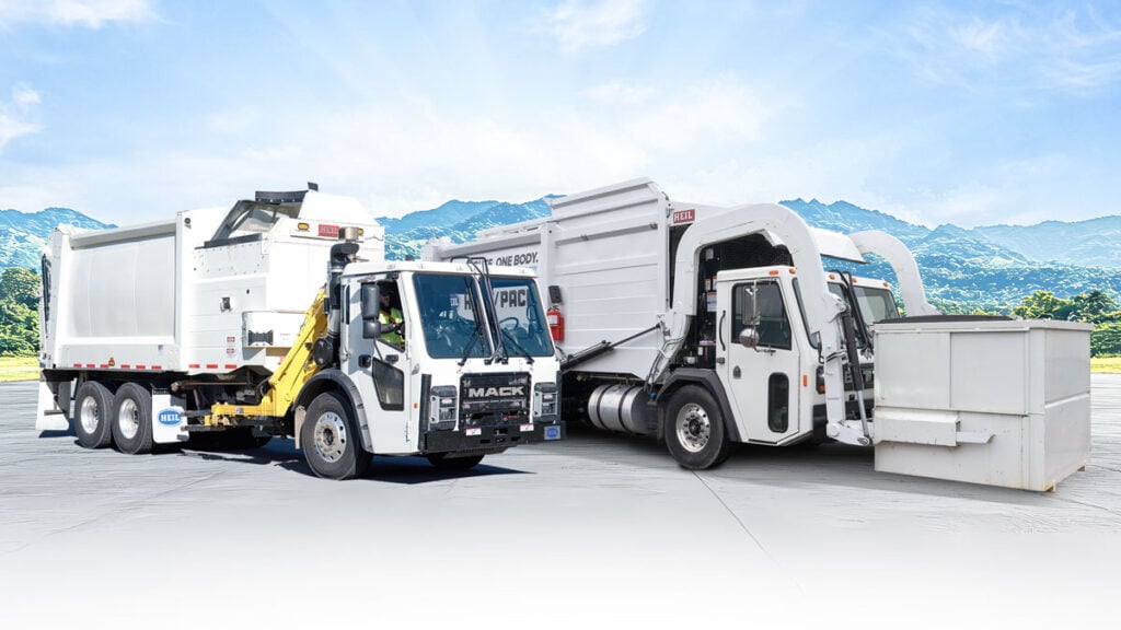Two white Mack refuse trucks with compactor bodies parked side by side outdoors