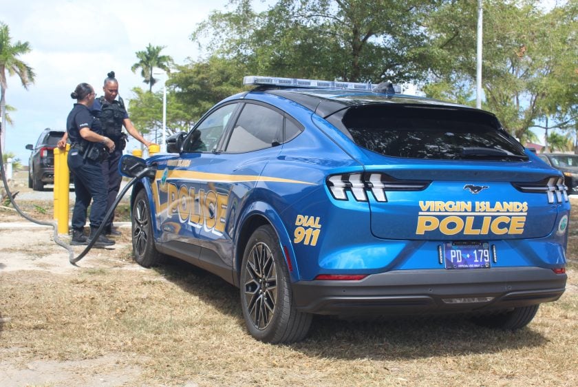 Virgin Islands Police Department officers stand beside blue and gold electric Ford Mustang Mach-E patrol vehicle