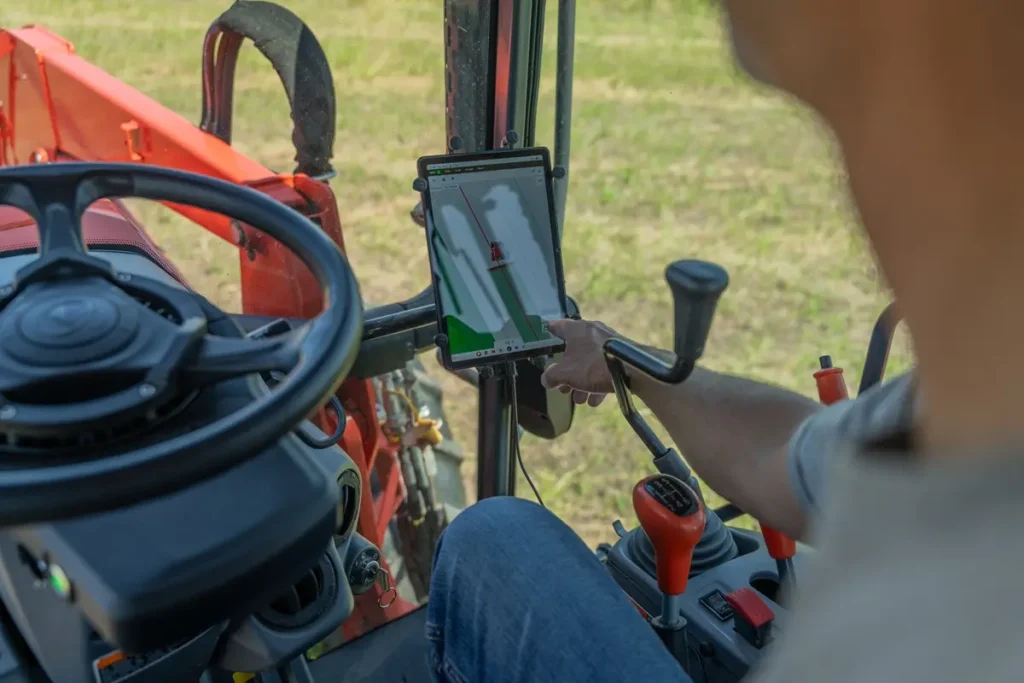 Operator in cab of red compact tractor using tablet mounted on steering column displaying autosteer guidance system