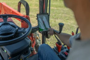 Operator in cab of red compact tractor using tablet mounted on steering column displaying autosteer guidance system