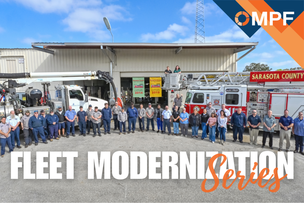 Large group of fleet personnel standing in front of fire trucks and maintenance facility building