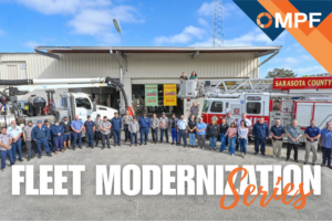 Large group of fleet personnel standing in front of fire trucks and maintenance facility building