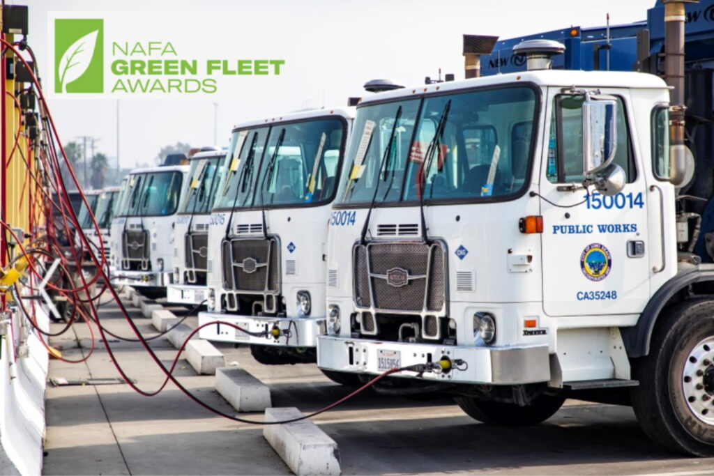 Row of white municipal utility trucks lined up at charging station with NAFA Green Fleet Awards logo