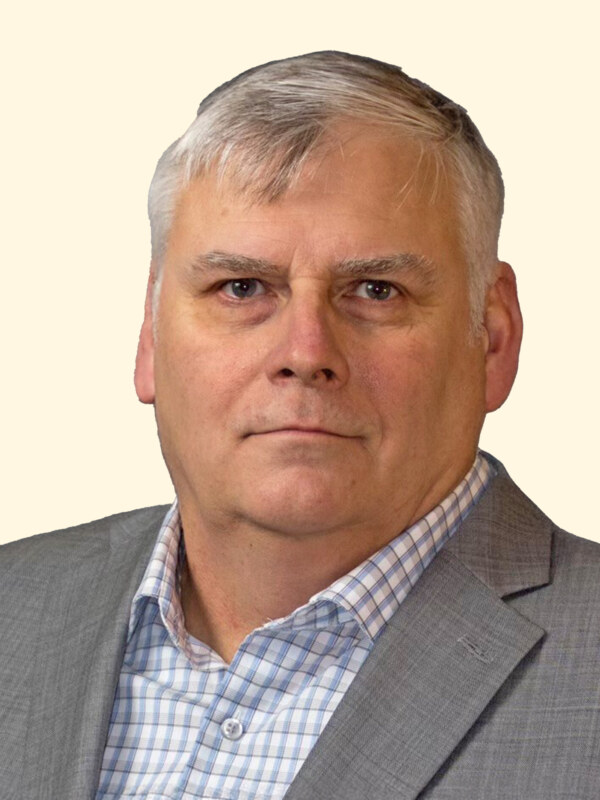 Professional headshot of middle-aged man in gray blazer and blue checkered shirt against neutral background