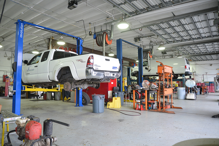 White pickup truck lifted on blue two-post vehicle lift in maintenance bay