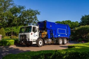 White and blue automated side-loader garbage truck parked on residential street