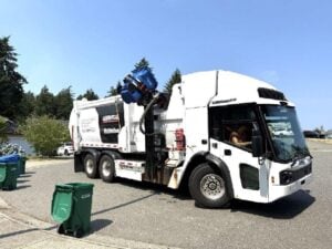 White refuse collection truck with hydraulic arm lifting green waste bin