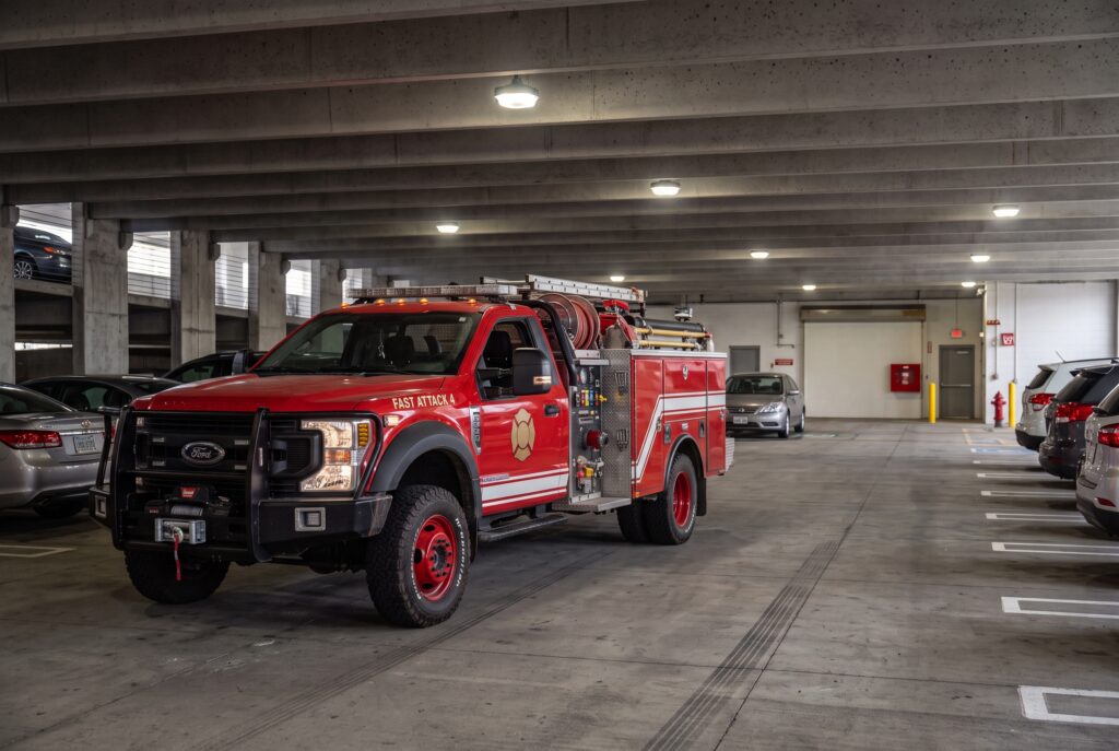 Red fire engine parked in underground garage with civilian vehicles nearby