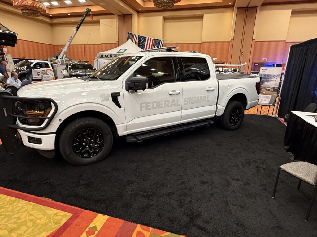 White pickup truck with "Federal Signal" text displayed at indoor trade show booth