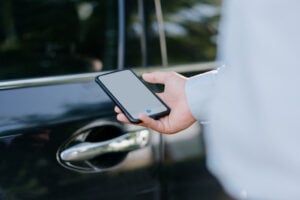 Person holding smartphone with blank screen beside white vehicle door and handle