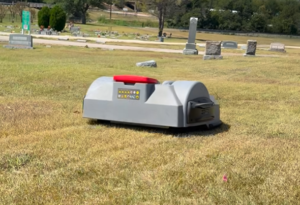 Robotic lawn mower operating in cemetery grounds with headstones visible in background