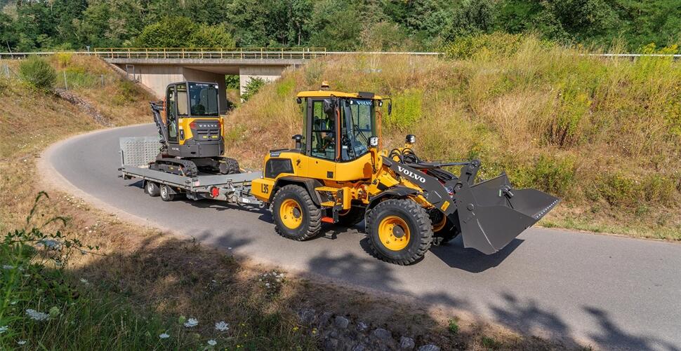 Yellow wheel loader and compact excavator on transport trailer in rural roadway setting