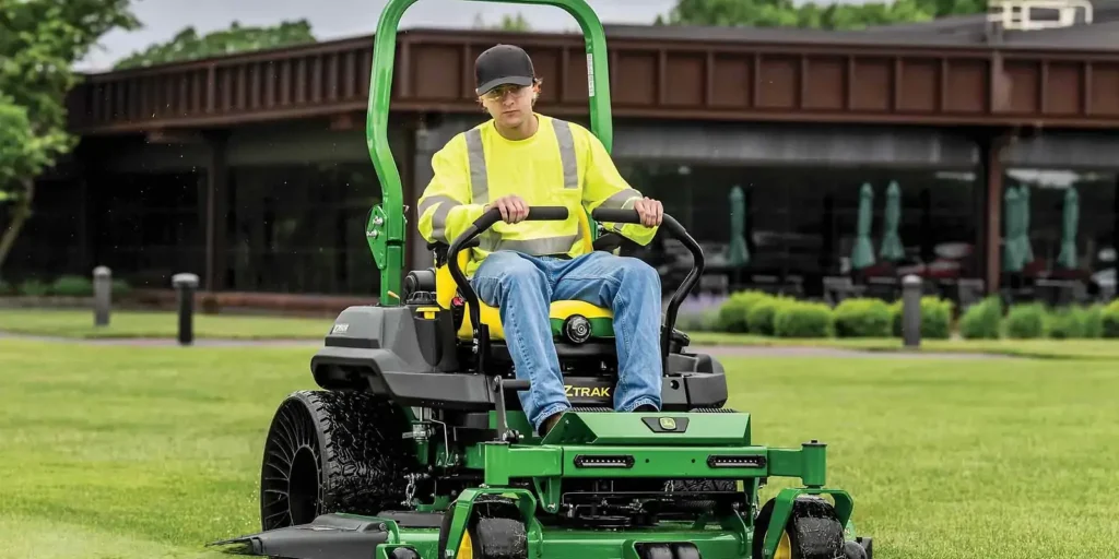 Operator in high-visibility vest on green zero-turn riding mower on manicured lawn