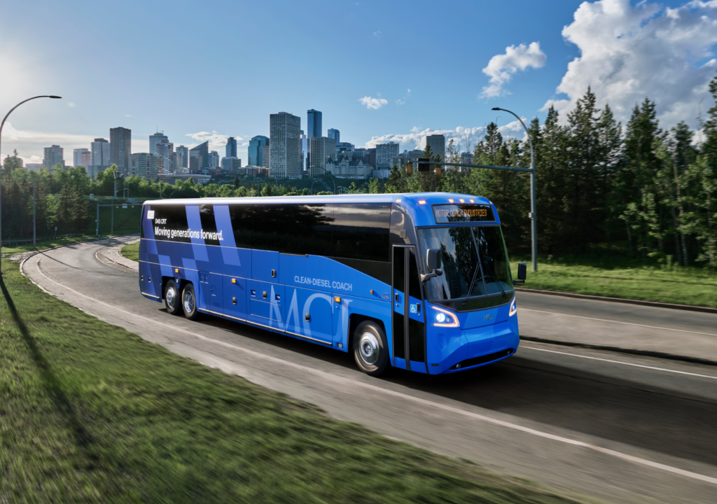 Blue commuter coach bus traveling on highway with city skyline in background