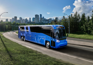 Blue commuter coach bus traveling on highway with city skyline in background