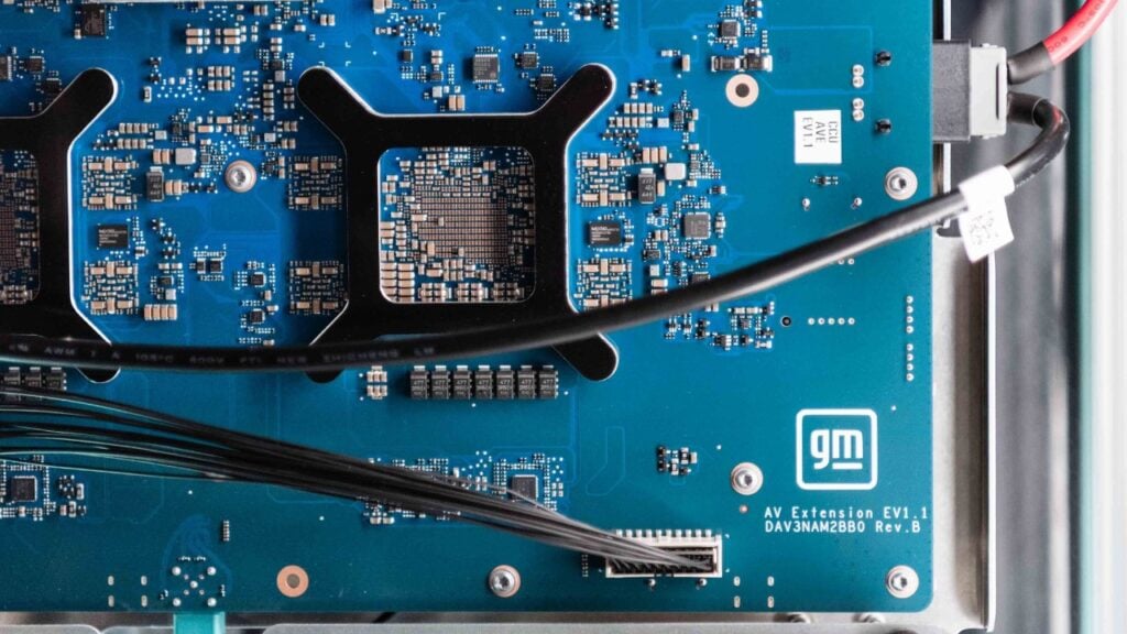 Close-up of blue circuit board with GM logo and integrated circuits, no trailing period