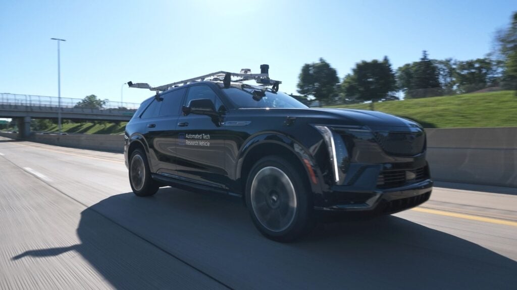 Black autonomous SUV with roof-mounted sensors driving on highway overpass