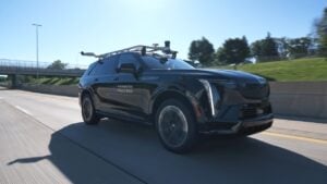 Black autonomous SUV with roof-mounted sensors driving on highway overpass