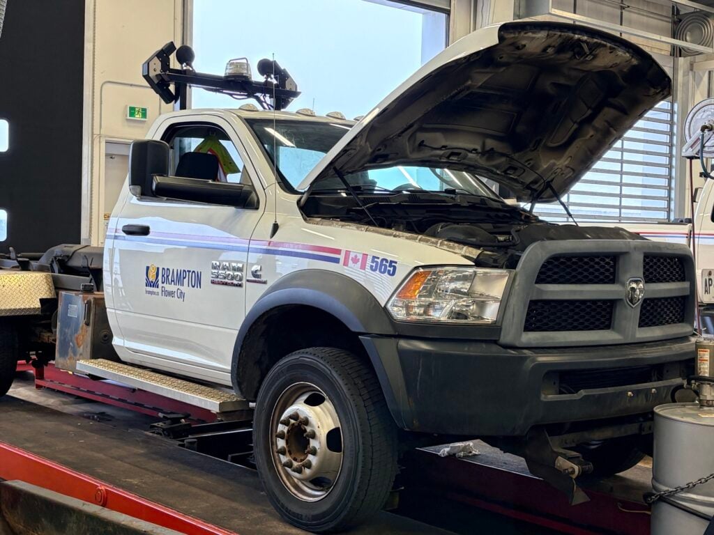 White Dodge pickup truck with open hood in service bay, Brampton branding visible on door