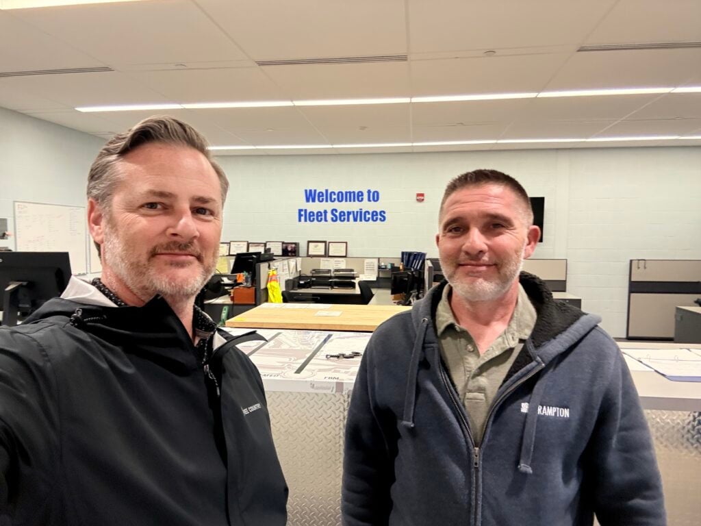 Two men in a Fleet Services office with signage and desks visible behind them