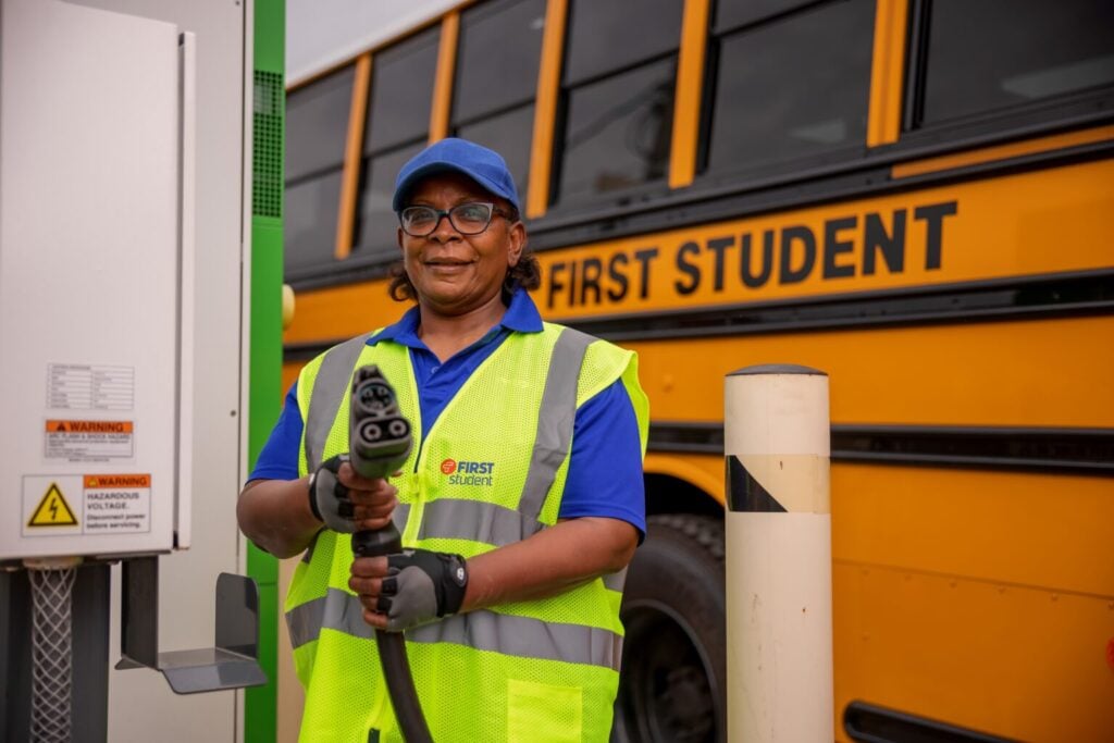 Worker in safety vest holding electric bus charging cable near yellow school bus