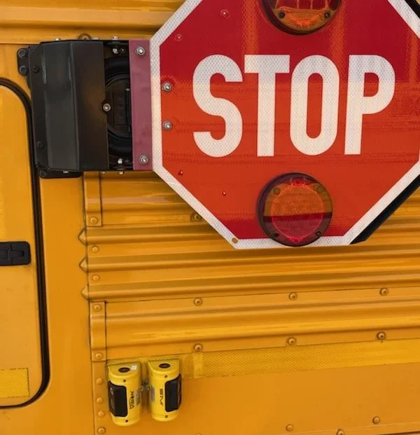 Close-up of school bus rear exterior showing STOP sign and electrical outlet mounted on yellow panel