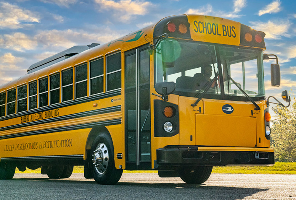 Yellow school bus with "School Bus" text visible on front, parked outdoors against blue sky
