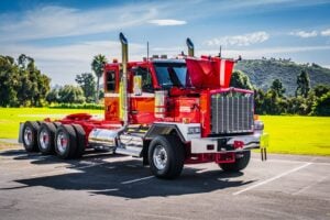Customized red semi-truck with chrome details parked in lot against green landscape