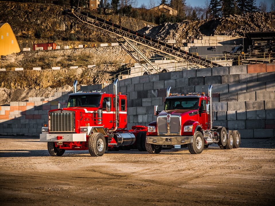 Two red heavy-duty dump trucks parked at construction site with aggregate stockpiles