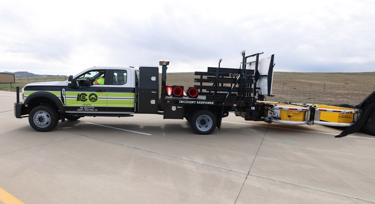 Green and white incident response truck with equipment trailer on rural highway