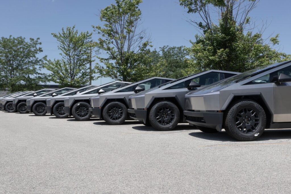 Row of six angular electric vehicles lined up in a parking lot with trees in background