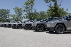 Row of six angular electric vehicles lined up in a parking lot with trees in background